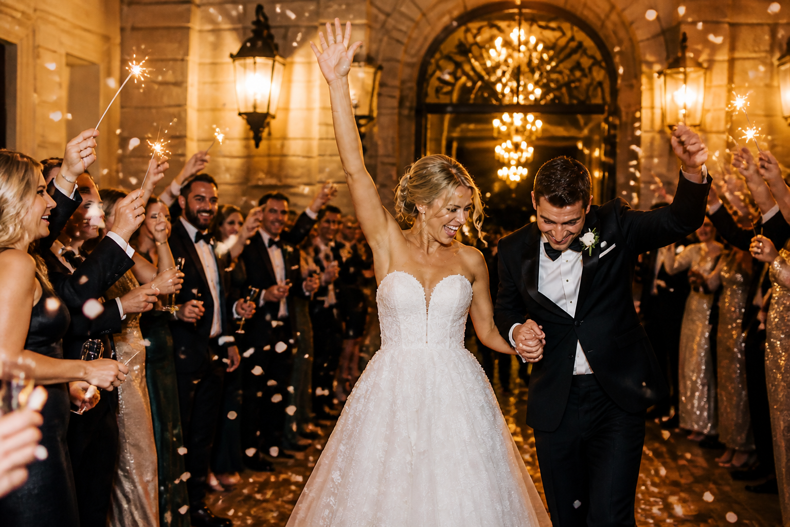 Newlyweds making their grand entrance into their wedding reception through a sparkler-lined crowd.